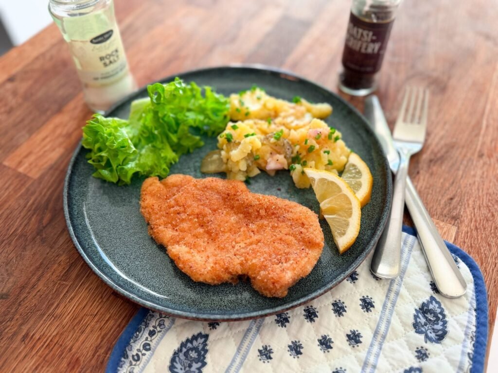 Wiener Schnitzel with Kartoffelsalat, lemon wedges and green salad on a dark plate