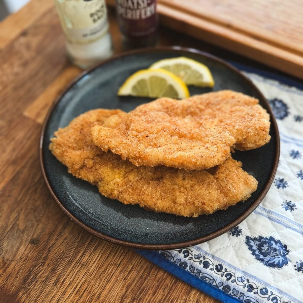 Two golden breaded Wiener Schnitzel on a dark plate with lemon wedges